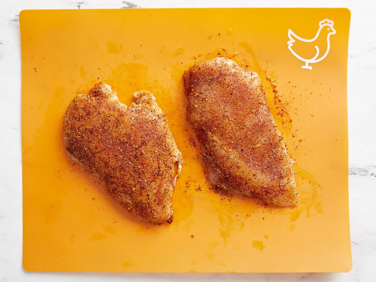 Seasoned chicken breasts on a cutting board.