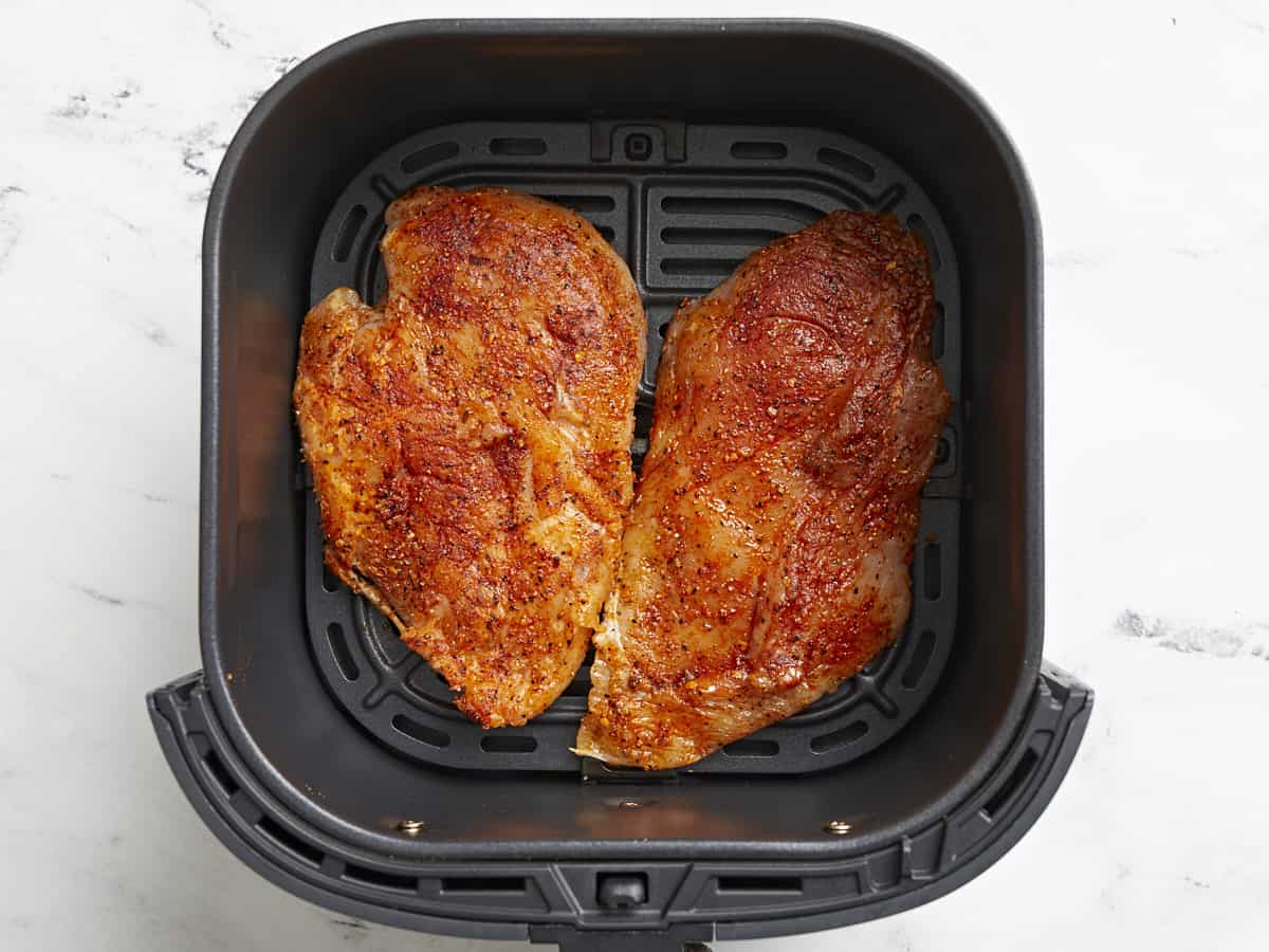 Uncooked chicken breasts added to an air fryer basket.