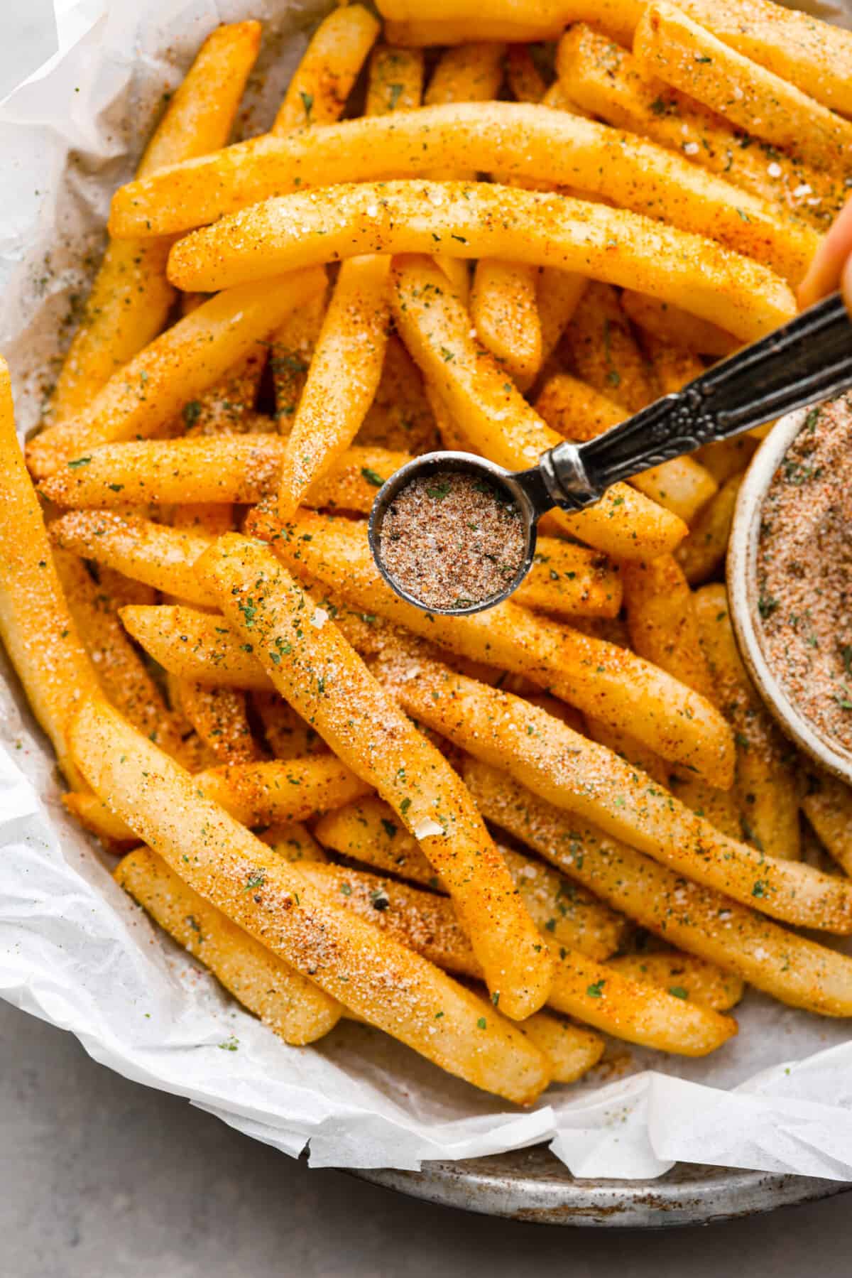 Fry seasoning being sprinkled on French fries.