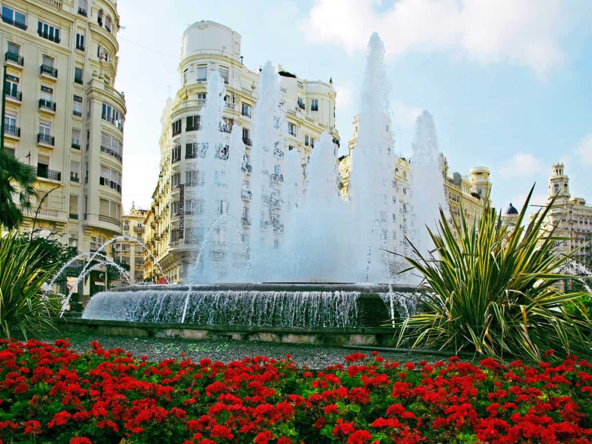 fountain surrounded by red flowers in plaza de ayuntamiento
