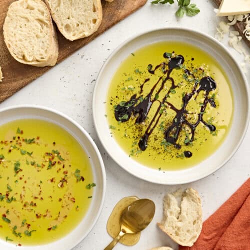 Hot honey dip and balsamic dip in white bowls on a white platter with bread and a spoon.