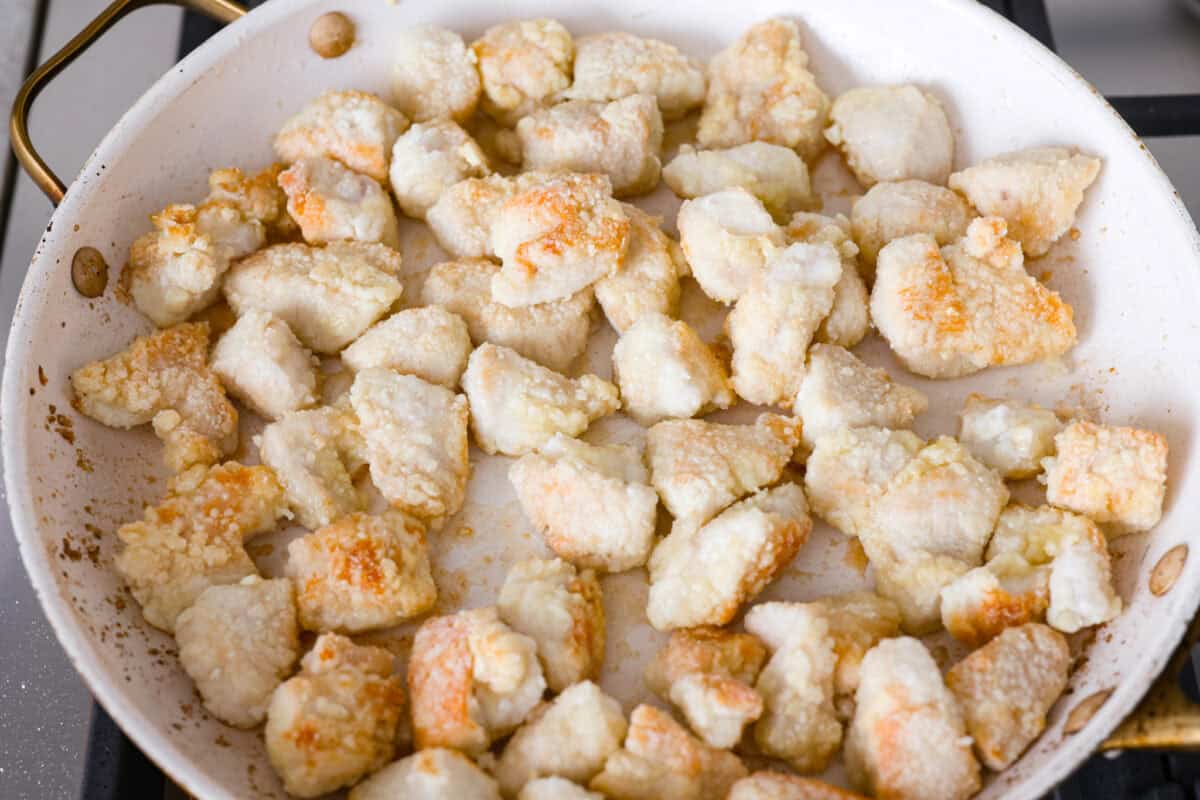 Cornstarch covered chicken cooking in a skillet on the stove.