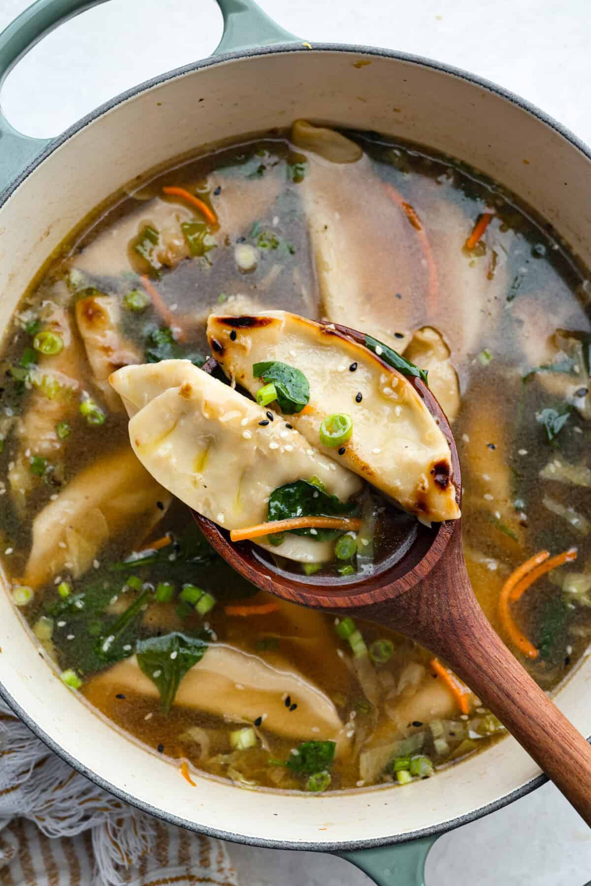 Overhead shot of someone scooping out some potsticker soup in a large wooden spoon.