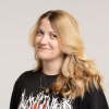 A photo portrait of a journalist with blonde hair and a band t-shirt.