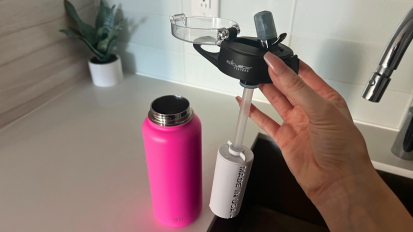Person holding water filter straw and lid over water bottle on countertop