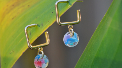 Gold earrings with recycled plastic charms hanging from plant leaf