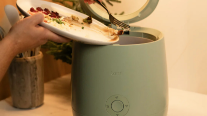 Person scraping food scraps into green Lomi on countertop