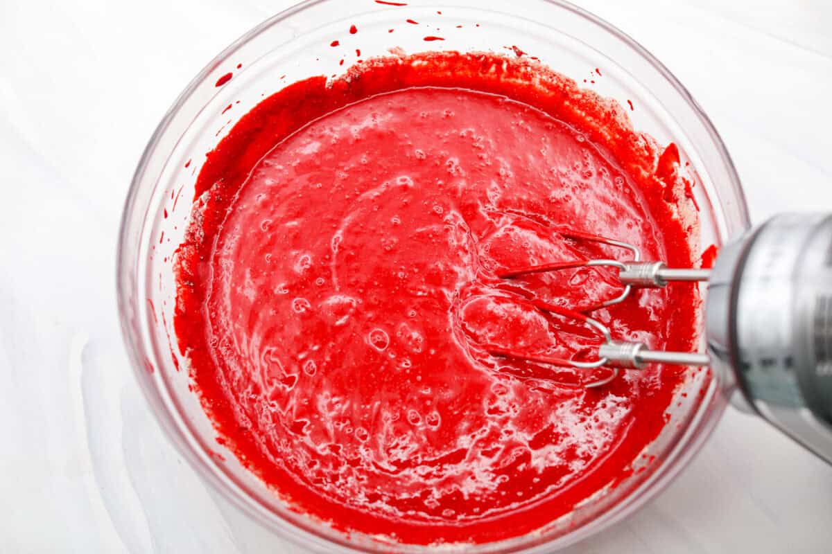 Someone using an electric hand mixer to mix the cake mix and soda together.