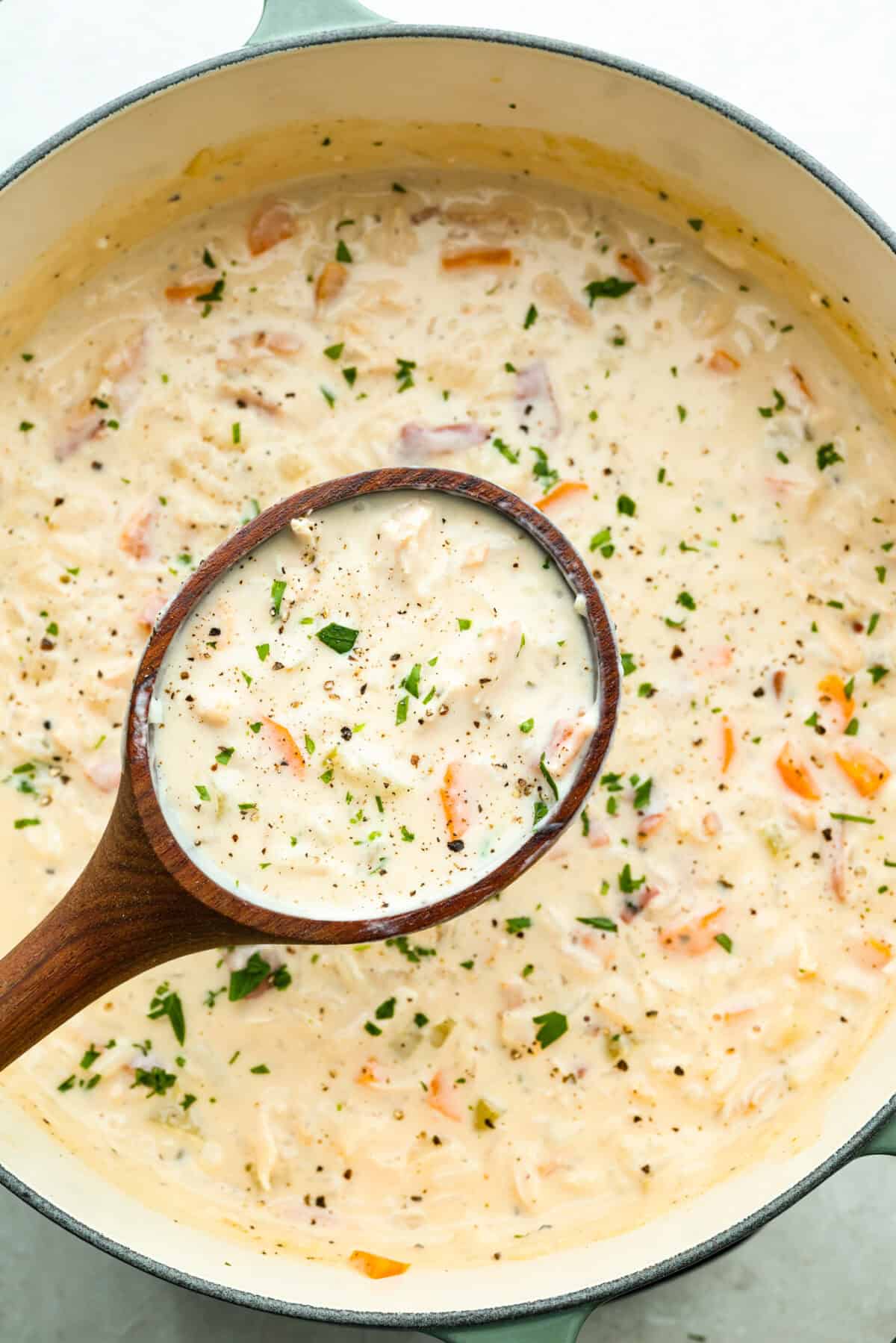 Stop what you are doing right now, and make this Crack Chicken and Rice soup! With tender chicken, rice, creamy cheese, crispy bacon, and bold ranch flavor, this easy one pot recipe tastes like pure comfort in every spoonful. Large pot of soup with a large wooden ladle lifting a scoop of crack chicken and rice soup out of the pot.
