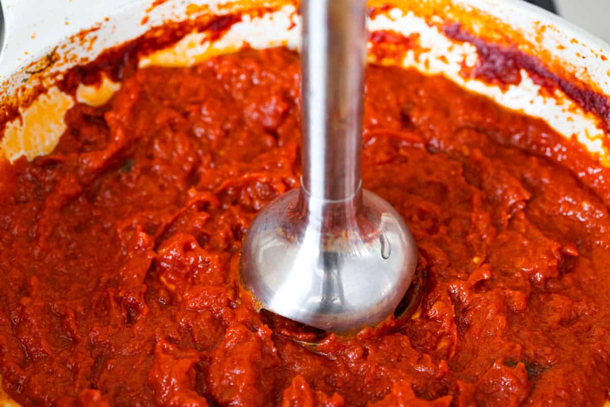 Someone using an emersion blender to blend up the sauce.