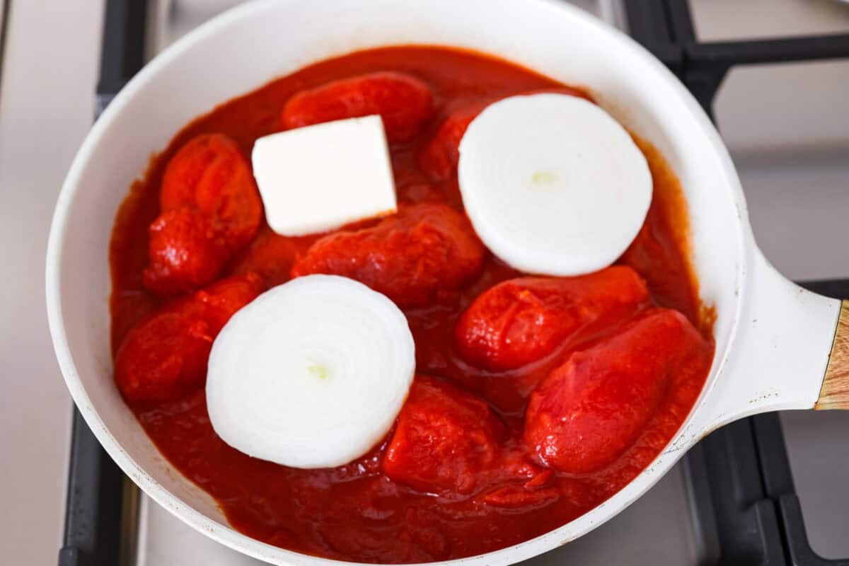 Tomatoes, onions, and nutter in a sauce pan on the stove.