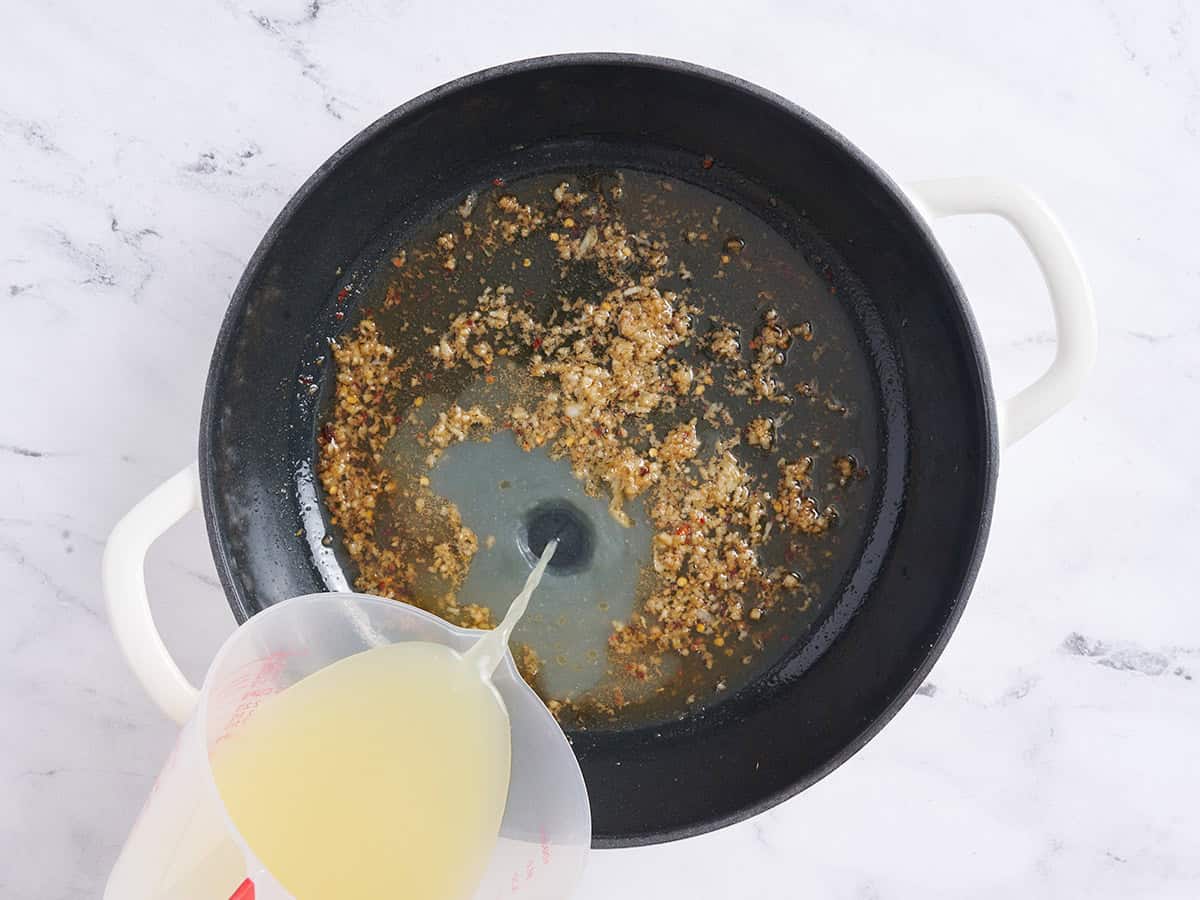 Brown being poured into browned minced garlic in a skillet.