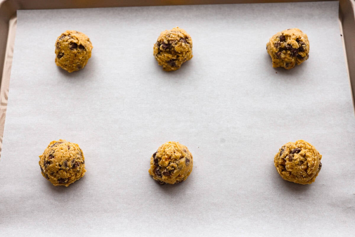 These Neiman Marcus Chocolate Chip Cookies come with a famous backstory, but the real star is the cookie itself. Thick, chewy, and packed with oats, two kinds of chocolate, and crunchy walnuts, they’re truly worth the hype. cookie dough balls added to a cookie sheet ready to be baked.