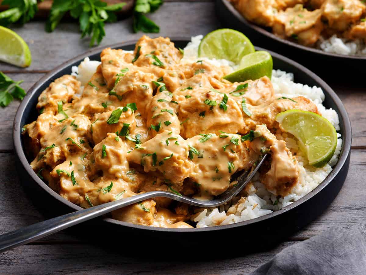 Side view of thai peanut chicken on a plate with white rice and lime rice and a fork.