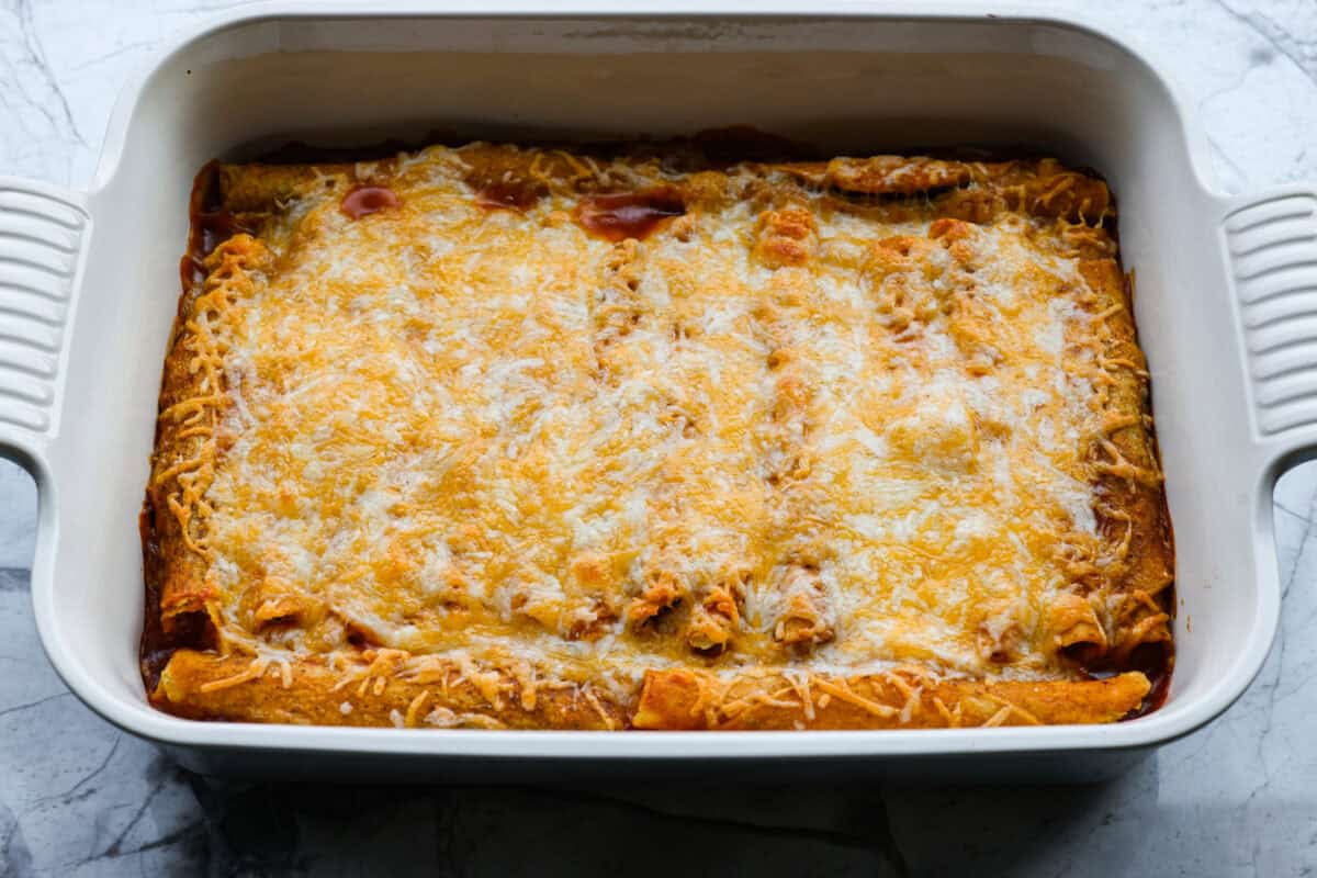 When you want enchiladas without the work, these Lazy Enchiladas are it! Four ingredients. Less than 30 minutes. Just layer frozen taquitos with beans, sauce, and cheese, bake until bubbly, and boom, dinner is served! Cheese spread over the top of the taquitos, baked and melted.