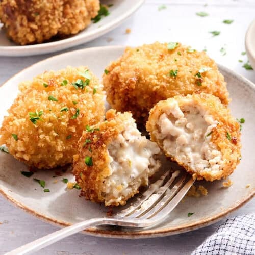Side view of chicken croquettes on a plate with one sliced in half.