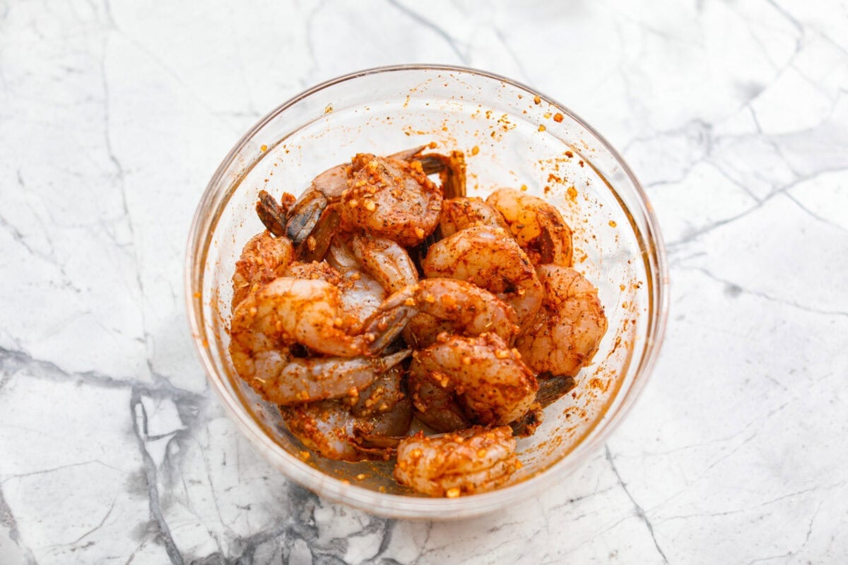 Raw shrimp covered in seasonings in a mixing bowl.