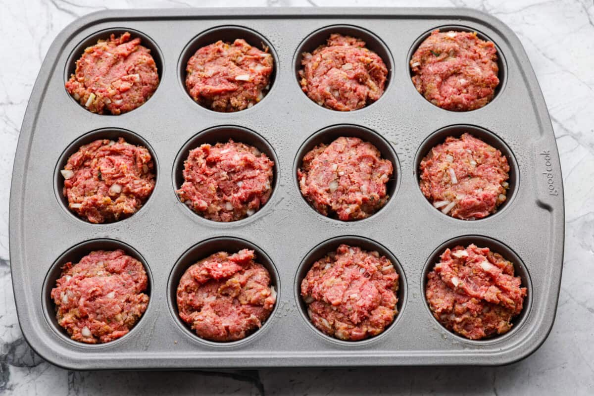 Mixed meatloaf mixtures separated into the muffin tins.