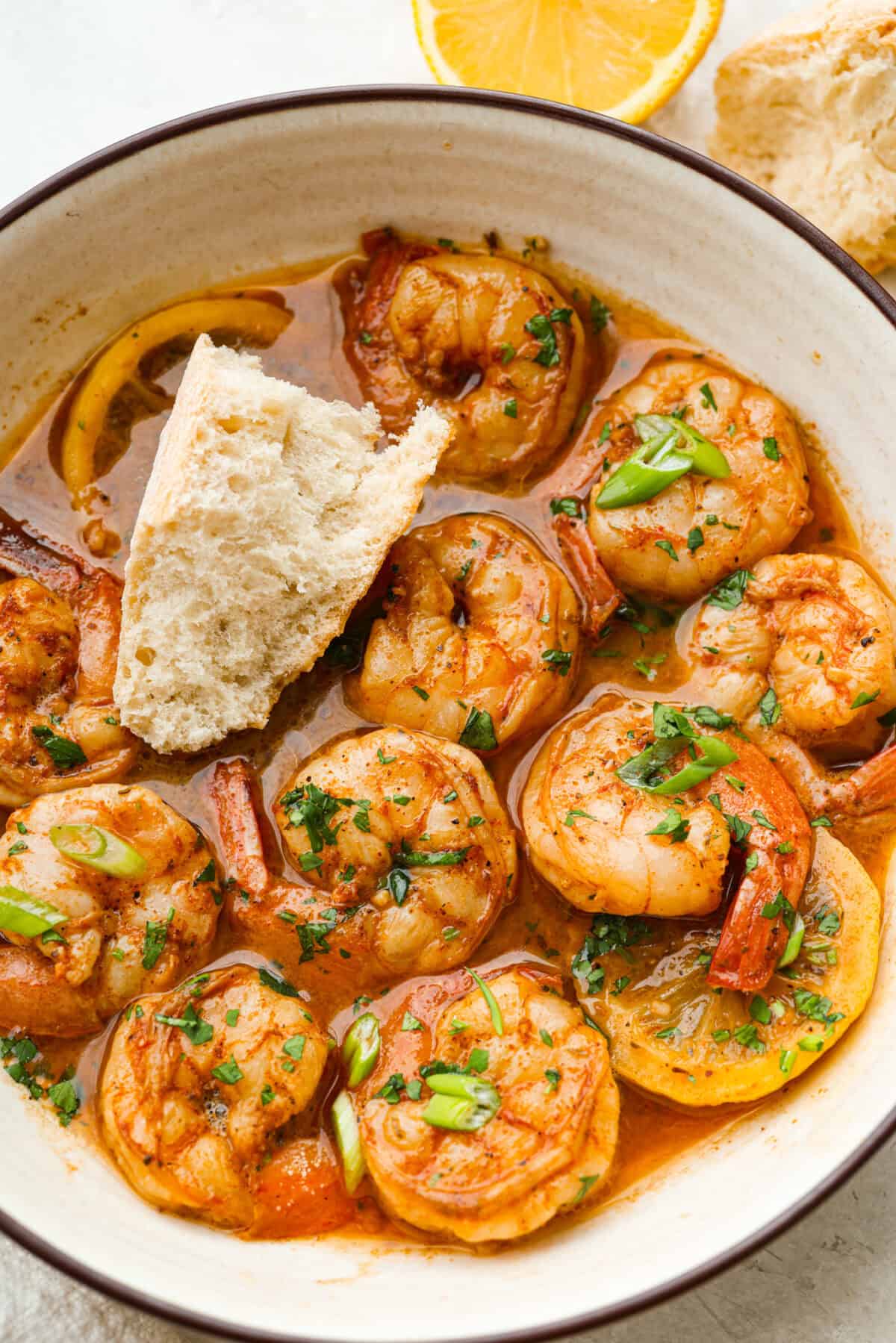 Plated New Orleans BBQ shrimp with a wedge of crusty bread.