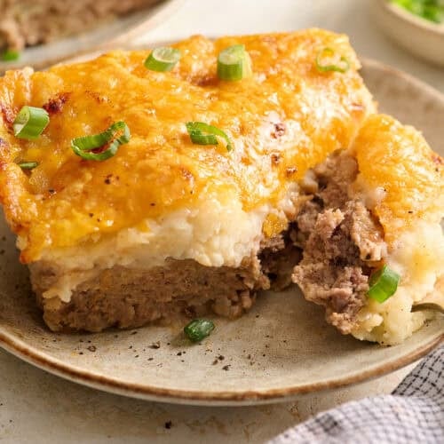 Side view of a slice of meatloaf casserole on a plate with a fork.
