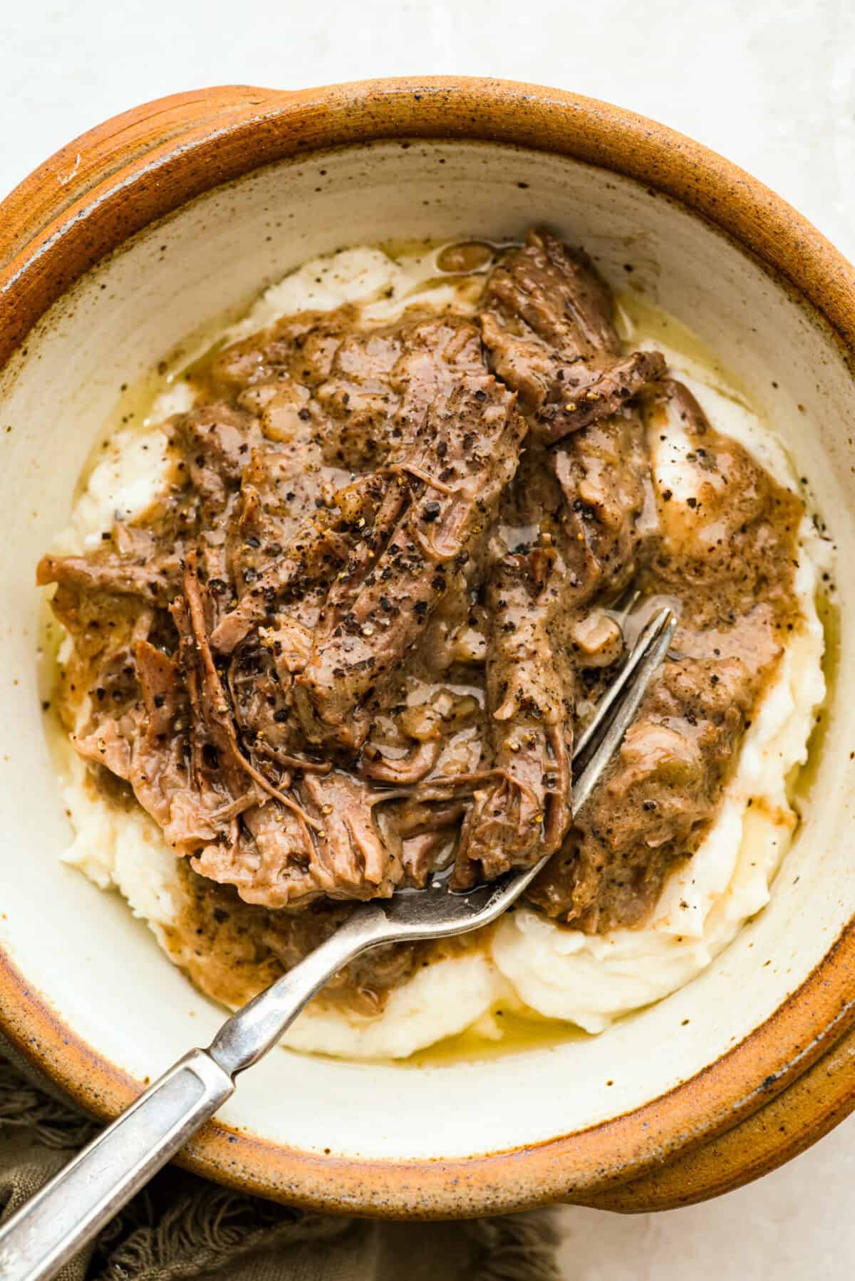 Serving of 4 ingredient mushroom beef in a bowl over mashed potatoes.