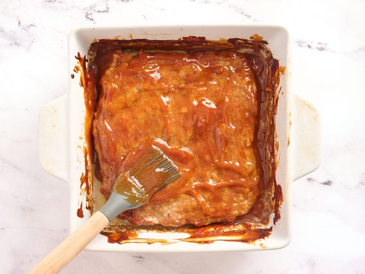 Meatloaf casserole being brushed with glaze after baking in the oven.
