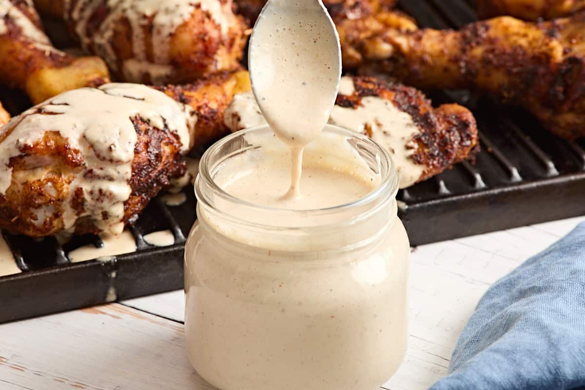 Homemade alabama white sauce in a glass mason jar with a spoon being pulled out covered in sauce.