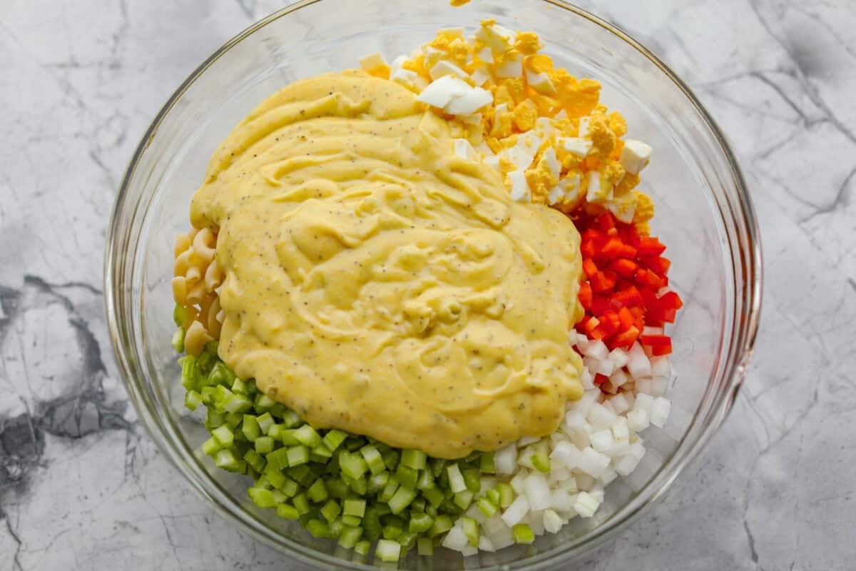 Dressing added to the bowl with pasta salad ingredients.