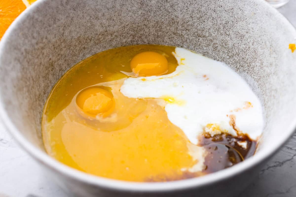 Wet ingredients added to the bowl of orange zest and sugar.