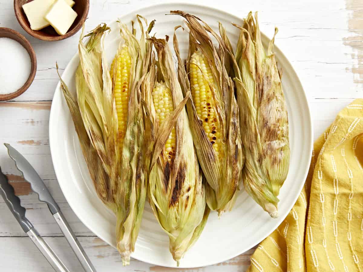 overhead view of 4 ears of grilled corn on a white plate.