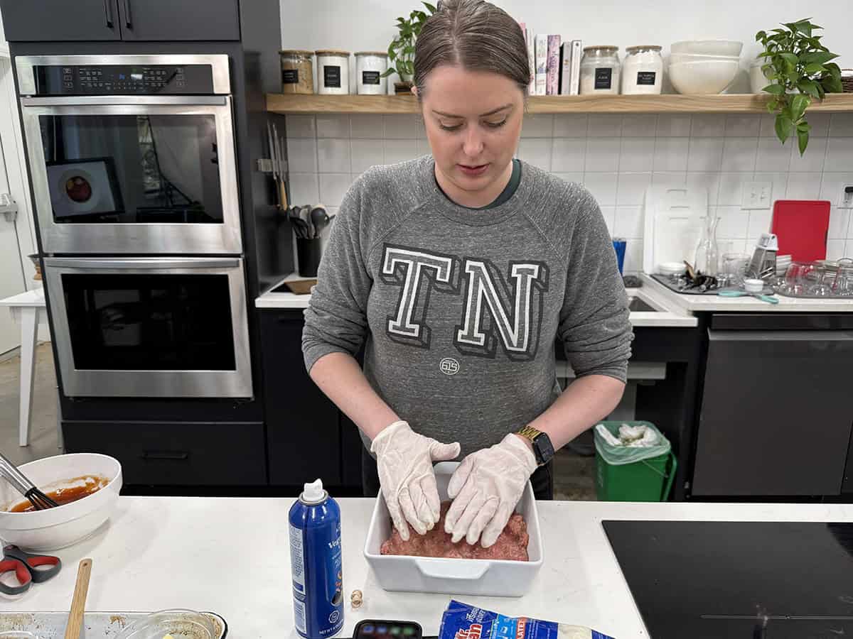 A woman pressing meatloaf mixture into a casserole dish.