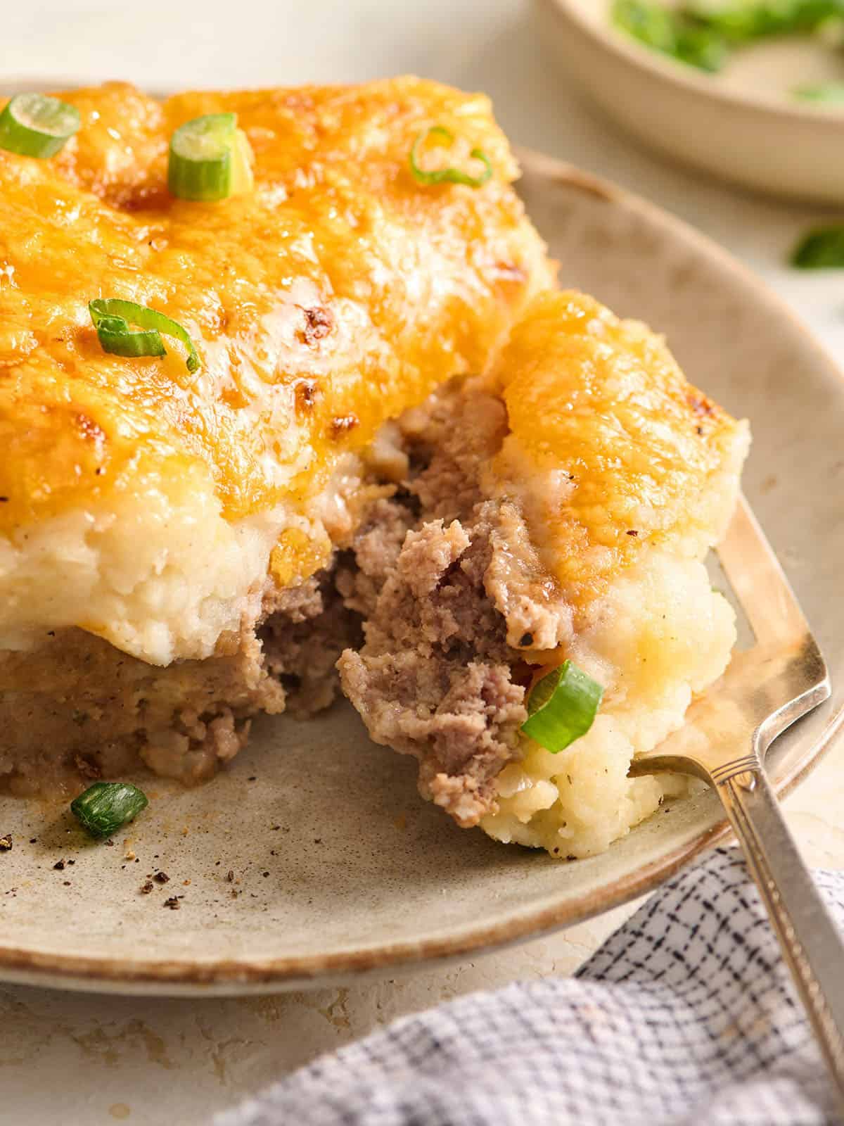 Side view of a slice of meatloaf casserole on a plate with a fork.