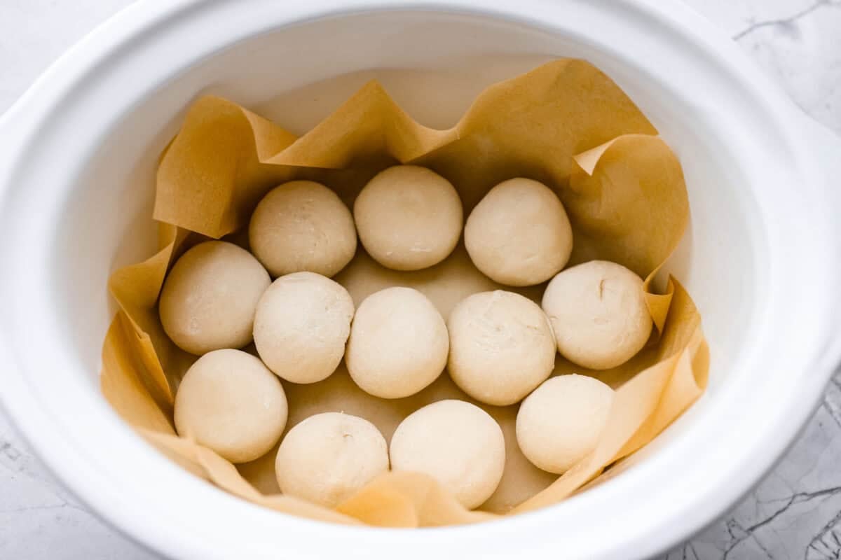 Frozen rolls on parchment paper at the bottom of the slow cooker.