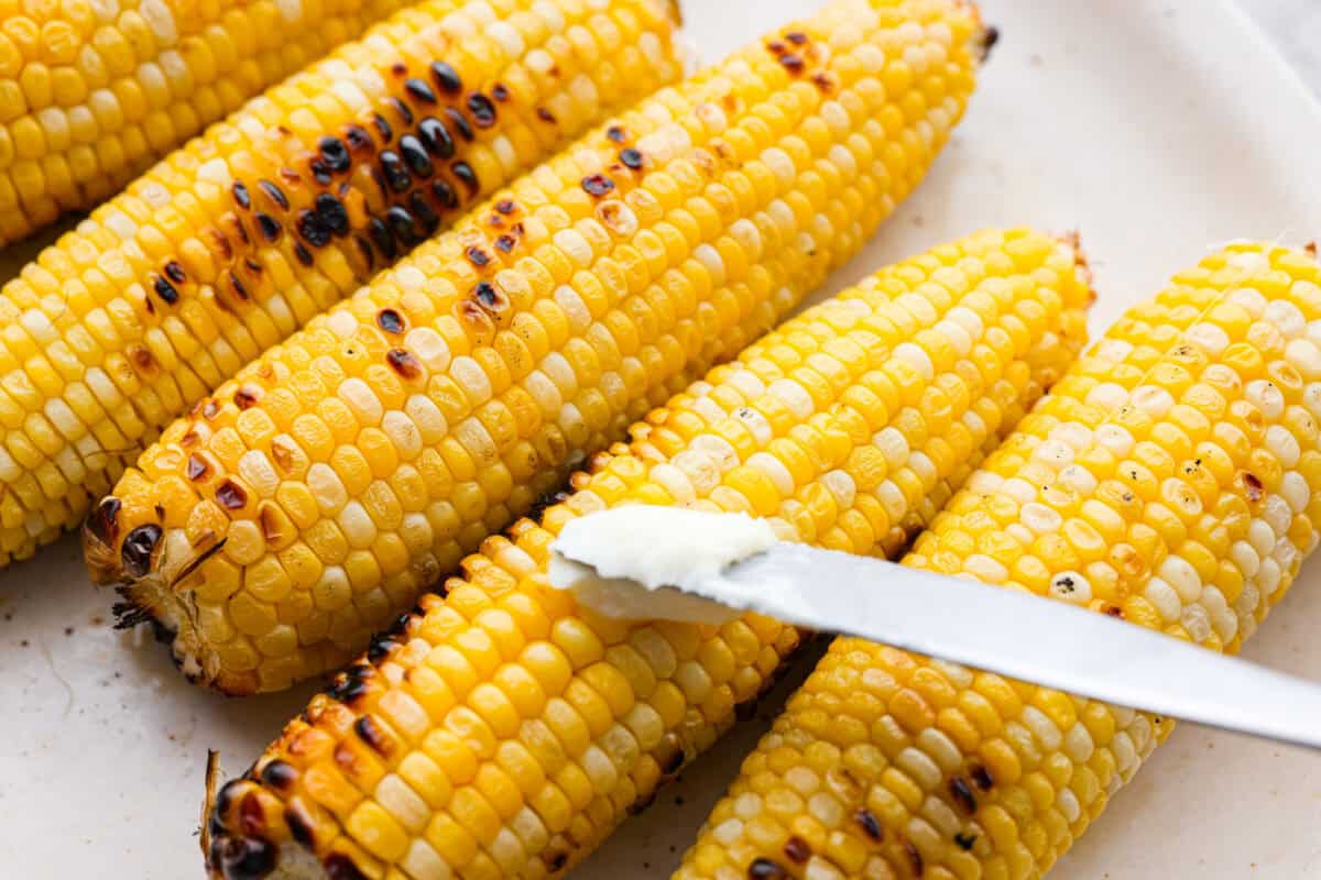 Someone spreading butter on the grilled corn.
