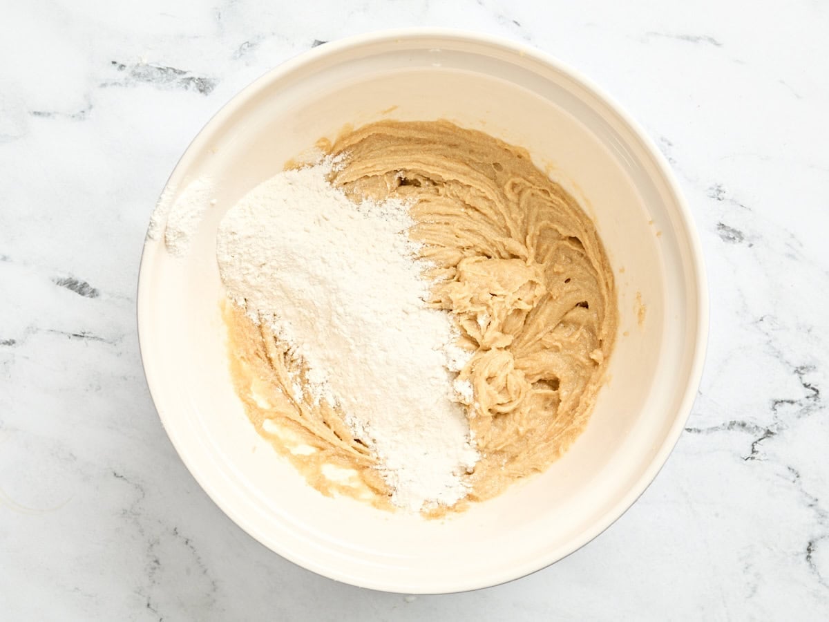 A little flour added to creamed butter, sugar and eggs in a bowl.