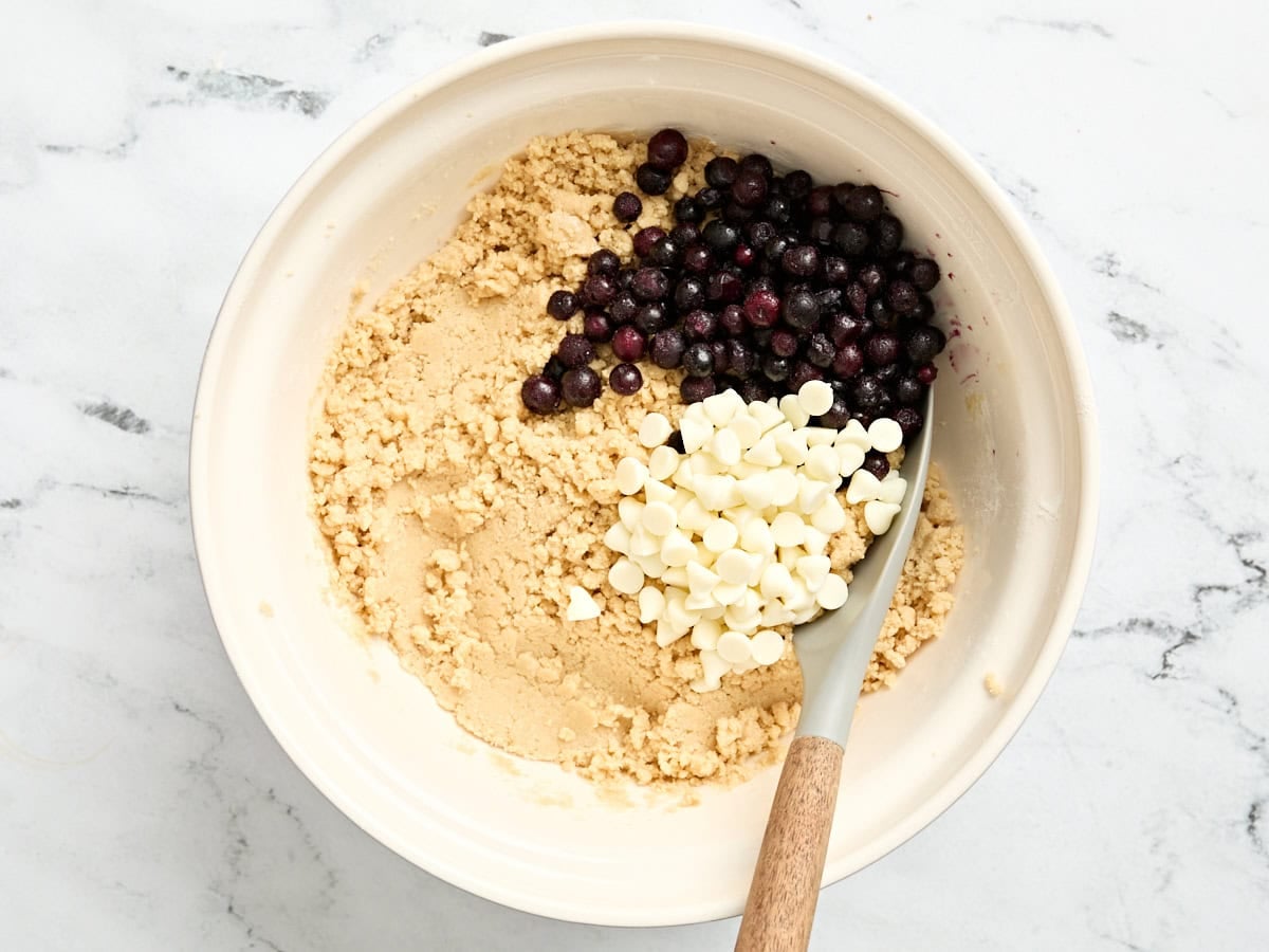 Blueberries and white chocolate chips added to a bowl of cookie batter.