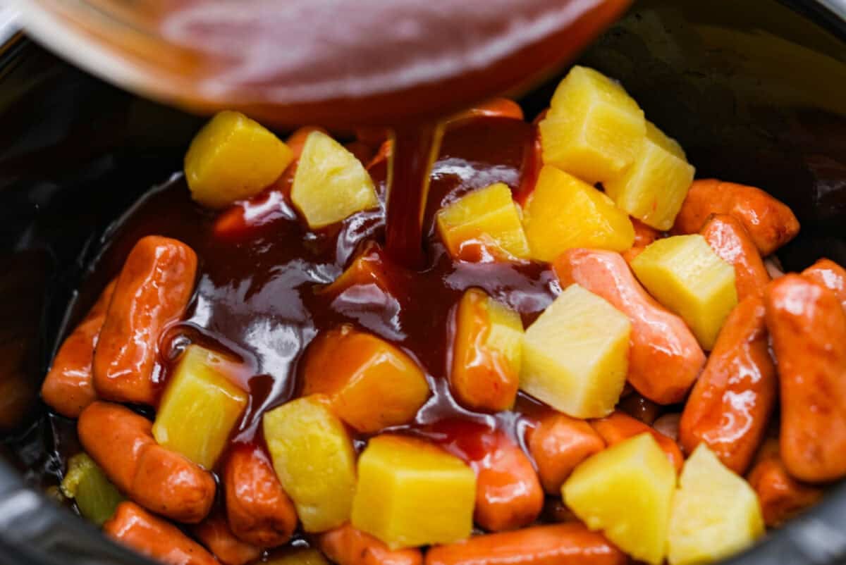 Sauce being poured over the pineapple and lit'l smokies in the slow cooker.