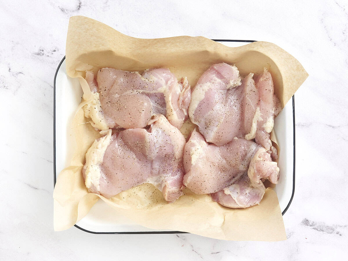 Chicken in a parchment lined baking dish topped with salt and pepper.