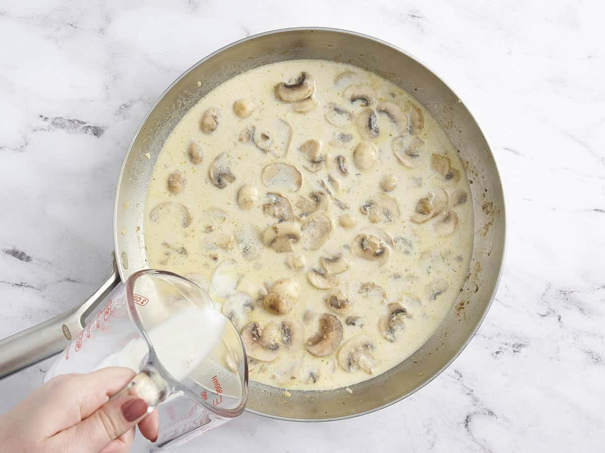Half and half being poured into a skillet with a creamy mushroom garlic pan sauce.