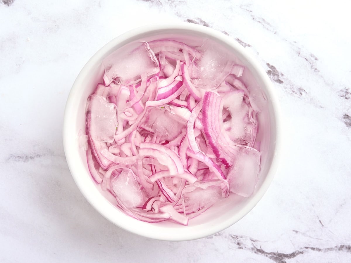 Sliced red onions in a bowl of ice water.