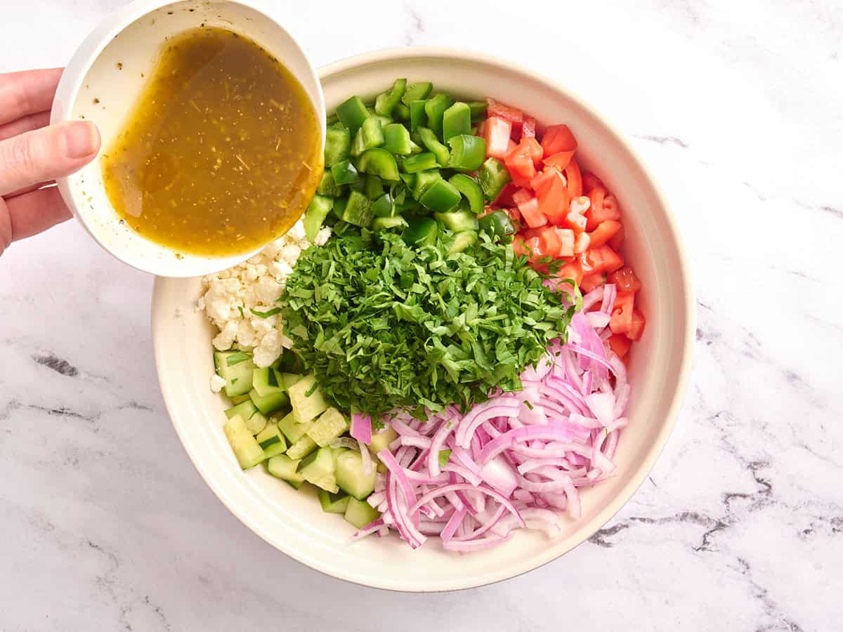 Cucumber tomato salad ingredients in a bowl with the dressing being poured over top.