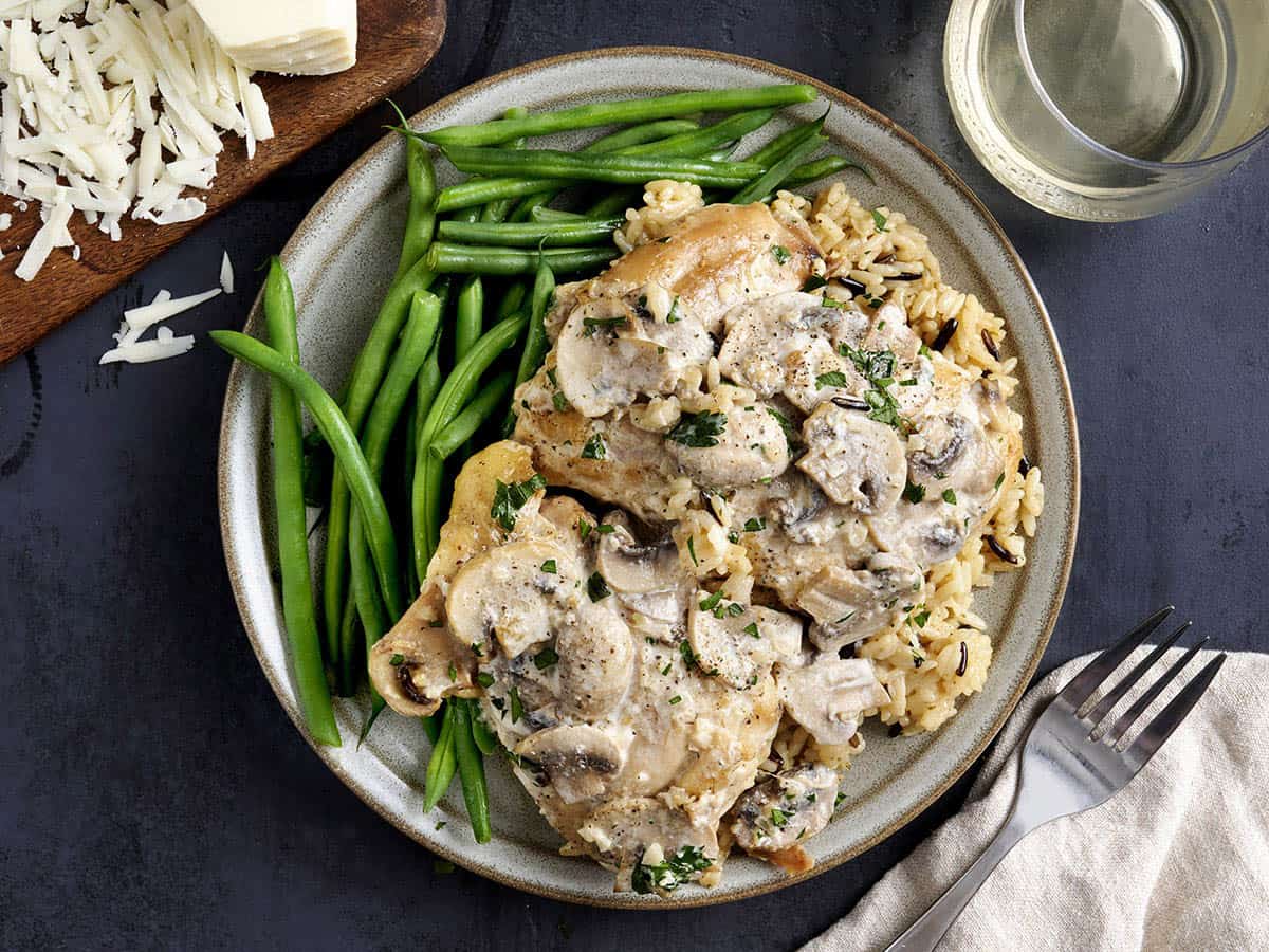 Overhead view of creamy mushroom chicken thighs on a plate with green beans.