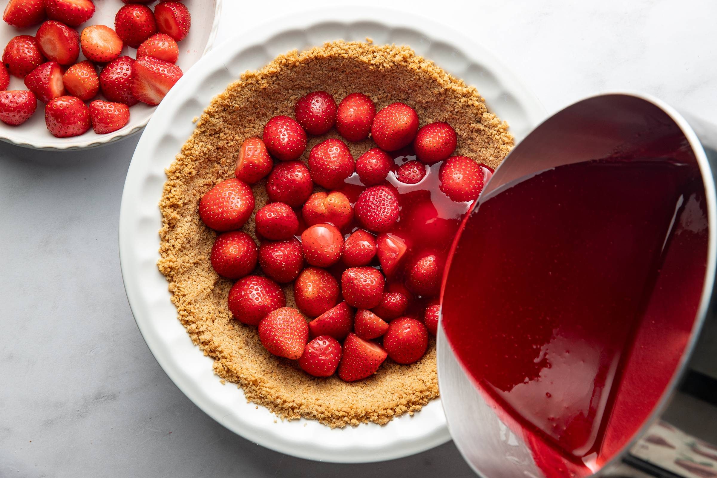 Pouring jello onto strawberries and pie crust.