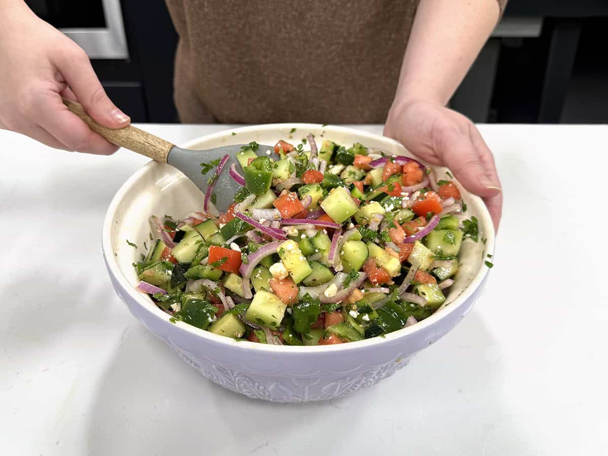 Front view of someone mixing a cucumber tomato salad in a bowl.