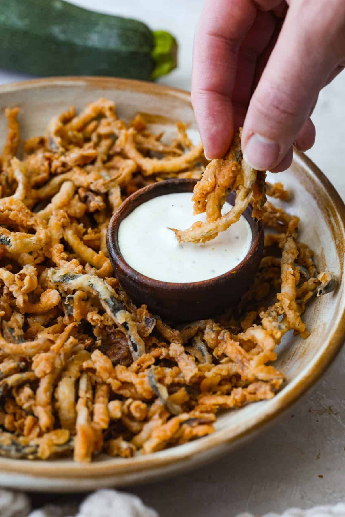 Someone dipping zucchini strings in ranch dressing.