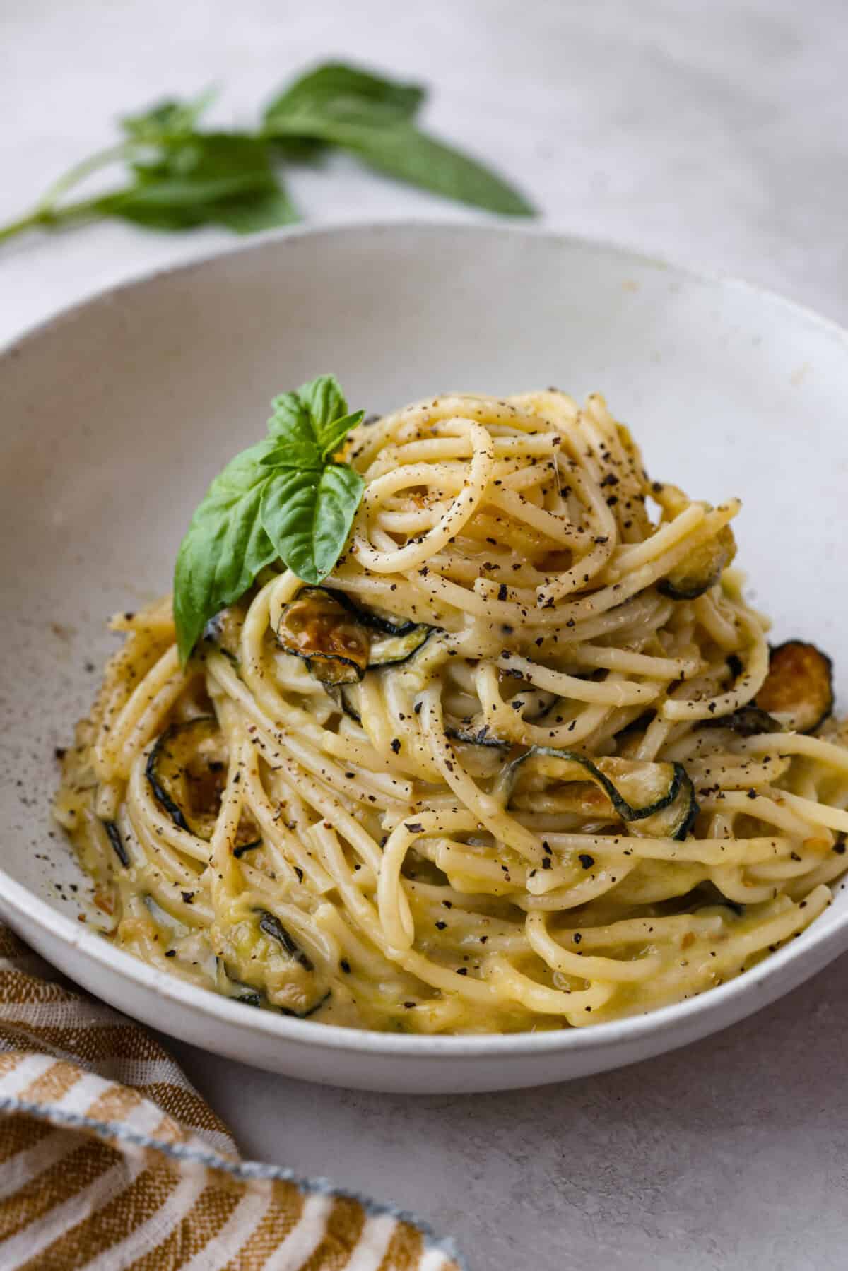 Spaghetti alla Nerano is an unforgettable pasta dish packed with flavor! It has a rich and creamy zucchini sauce infused with garlic, fresh basil, and melted cheese. Close view of a pile of spaghetti alla Nerano in a white bowl garnished with fresh basil.
